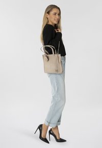 Bolso tote de cuero beige con doble asa y detalle de logo, combinado con jeans de denim azul claro remangados y tacones altos negros.