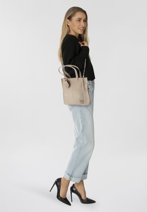 Borsa tote in pelle beige con doppi manici e dettaglio con logo, abbinata a jeans in denim azzurro arrotolati e tacchi alti neri.