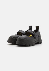 Black leather shoes with a rounded toe, adjustable strap, and chunky, ridged sole. Inside features a contrasting yellow lining.