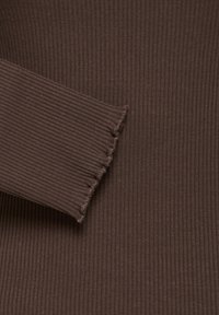 Gros plan d'un tissu côtelé marron avec une manche présentant un détail d'ourlet à bord ondulé.