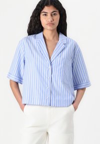 Kurzärmeliges Crop-Shirt in Hellblau mit weißen vertikalen Streifen, ausgestattet mit einem Kragen, Knopfverschluss und einer Brusttasche. Glatter Stoff. 