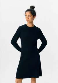 Schwarzes, geripptes Strickkleid mit Rundhalsausschnitt, langen Ärmeln und seitlichem Schlitz. Die glatte Textur und das taillierte Design sorgen für eine schlanke Silhouette.