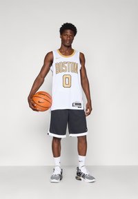 Witte basketbalshirt met "BOSTON" in goud, nummer "0", gecombineerd met zwarte shorts met witte rand. Houdt een basketbal vast, draagt sneakers.