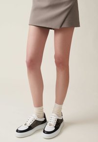 Sneakers con un design bianco e nero, tessuto testurizzato sui lati, hardware dorato e suola bianca, abbinate a calzini color crema.