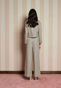 Ruuduline jumpsuit beežis, kollases ja sinises; talje kohandatud ülemise osaga, pikad varrukad ja laiad püksid. Sile kangas, pahkluuni ulatuv äär.