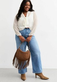 Weiße Bluse mit Bindetail, hellblaue High-Waist-Jeans, braune Fransen-Handtasche und beigefarbene spitze Pumps. Glatter Stoff und lockere Passform.