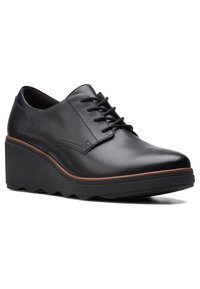 Chaussure compensée en cuir noir avec lacets à l'avant, garniture marron au-dessus de la semelle épaisse, et semelle extérieure texturée pour une meilleure adhérence.