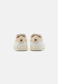 Witte leren sneakers met een zachte beige accent op de hiel, een gestructureerde rubberen zool en een minimalistisch ontwerp. Gouden hardware detail op de hiel.