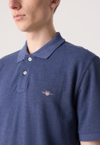 Marineblaues Polohemd aus strukturiertem Stoff mit einer Knopfleiste mit zwei Knöpfen und gesticktem Logo auf der linken Brust. Kurzärmlig.
