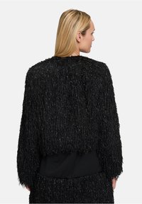 Schwarze Texturjacke mit einem struppigen, fransigen Design, das einen weichen, reflektierenden Faden enthält. Kurz geschnitten, mit langen Ärmeln und einer einfarbigen Rückseite.