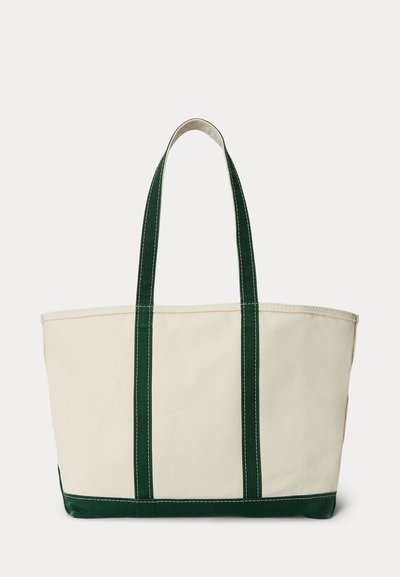 Beige canvas tas met donkergroene handvatten en biezen, rechthoekige vorm, open bovenkant en zichtbare stiksel details.