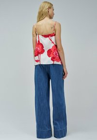 Camiseta floral en tejido blanco con estampado de flores rojas, combinada con pantalones vaqueros de pierna ancha en azul con dobladillo y una textura sutil.