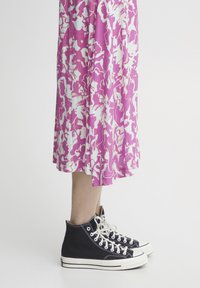Zapatillas altas negras con detalles blancos combinadas con un vestido de estampado floral en rosa y blanco, que exhibe un diseño elegante y casual.
