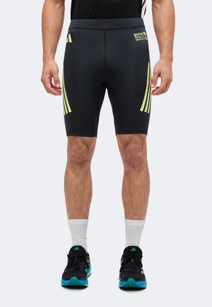 Mann trägt schwarze, enganliegende Laufshorts mit gelben Streifen und BMW Berlin Marathon-Logo, weiße Socken und schwarze Laufschuhe mit blau-grünen Sohlen.