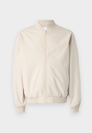 Chaqueta bomber beige con cremallera frontal, cuello y puños acanalados, tela suave y bolsillos laterales. Diseño simple con un corte relajado.