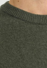 Suéter de punto verde oscuro con cuello redondo acanalado. La textura es suave con un tejido consistente y uniforme en toda la tela.