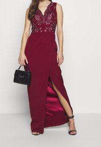 Burgundy aftonklänning med blommig spets överdel, djup V-ringning och en sidoklyfta. Bärs med en svart strukturerad handväska och sandaler med remmar.