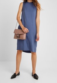 Blå ärmlös klänning med avslappnad passform, i kombination med en ljusrosa handväska med cirkulär beslag och svarta slip-on skor.