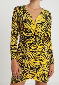 Šaty s potiskem zebra v žluté a černé barvě, s dlouhými rukávy a výstřihem do V. Mají zavinovací design a na bocích drapérie v pase. Měkká struktura látky.
