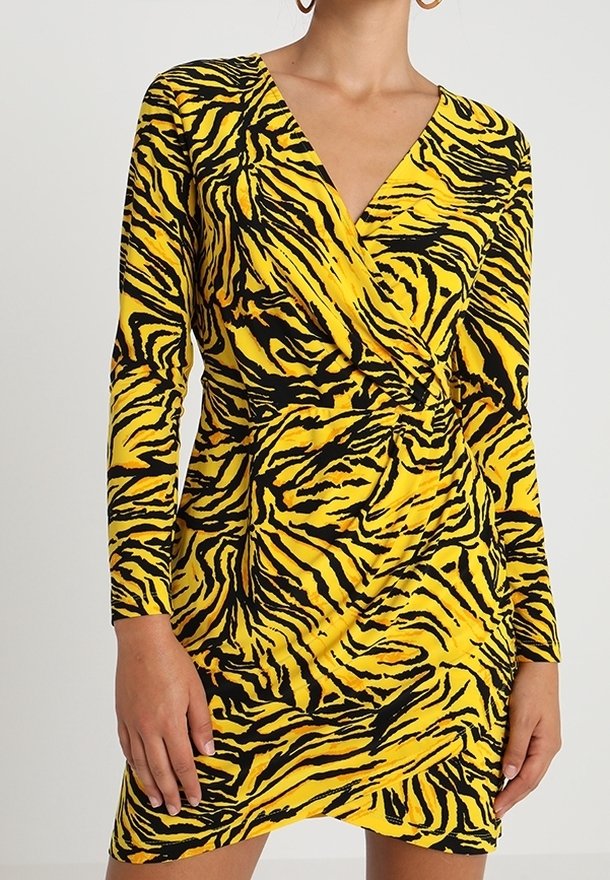 Šaty s potiskem zebra v žluté a černé barvě, s dlouhými rukávy a výstřihem do V. Mají zavinovací design a na bocích drapérie v pase. Měkká struktura látky.