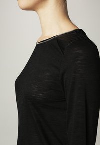 Czarny top z długim rękawem, okrągłym dekoltem i srebrnym zamkiem błyskawicznym. Posiada teksturowane ramiona oraz miękki, lekki materiał.