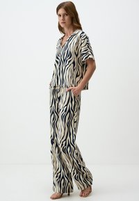 Twee-delig outfit in beige met marineblauwe zebra strepen; shirt met korte mouwen en kraag en losse broek met zakken.