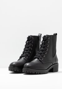 Bottes noires en cuir à la cheville avec un bout arrondi, fermeture à lacets à l'avant, fermeture éclair latérale, et semelle en caoutchouc épaisse avec une semelle crantée prononcée.