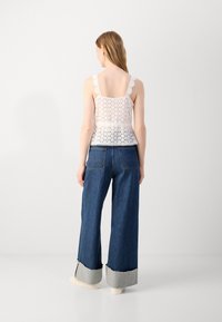 White lace top with scalloped straps, paired with wide-leg blue denim jeans featuring a gray cuff at the hem. Back view only.