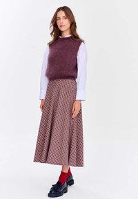 Žena v bielej dlhoprstovej košeli, fialovej chlpaté bezrukávovej svetri, červeno-bielej kárované sukni, červených ponožkách a čiernych mokasínach.