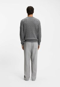 Grauer Kabelstrickpullover mit gerippten Bündchen und Saum, kombiniert mit hellgrauen, weit geschnittenen Hosen mit einer Gesäßtasche.