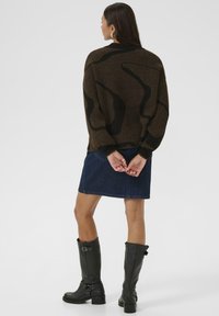 Brown sweater with abstract black pattern, paired with a denim skirt. Black knee-high boots with buckles complete the outfit.