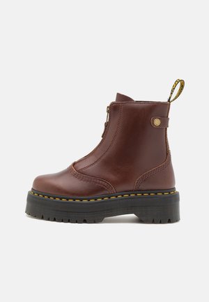 Bottine en cuir marron avec semelle noire épaisse, coutures jaunes, fermeture éclair latérale et languette de tirage brandée au talon.