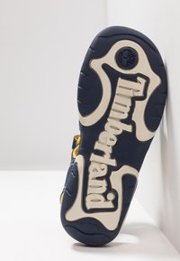 Mörkblå sneakersula med vitt "Timberland"-logotyp, texturerat gummimaterial, icke-märkande grepp och rundad form vid tån.