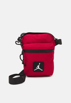 Bolso cruzado de nylon rojo con una correa negra, que presenta un bolsillo frontal y un logotipo Jumpman blanco en un parche cuadrado negro.