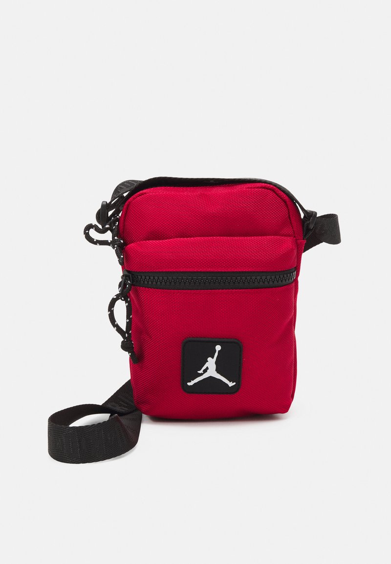 Borsa a tracolla rossa in nylon con una tracolla nera, dotata di una tasca frontale e un logo Jumpman bianco su un'etichetta quadrata nera.