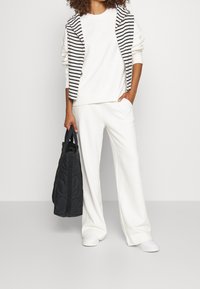 Witte outfit bestaande uit een sweatshirt en wijde broek, gecombineerd met een zwarte doorgestikte handtas. De hoodie heeft een zwart-wit gestreept ontwerp.