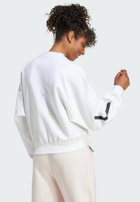 Biela mikina s uvoľneným strihom, rebrovaným lemom a pre veľké rukávy. Obsahuje kontrastný čierny pruh na ramene a mäkkú textúru.
