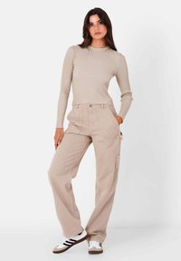 Beige geribde lange mouw top gecombineerd met losse beige cargobroeken met voorzakken. Gestyled met witte sneakers met zwarte strepen.
