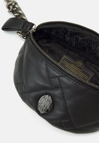 Musta nahkalaukku, jossa tikattu kuvio, hopeaketjusta valmistettu olkahihna ja koristeellinen hopeinen sulkaneula edessä. Sisäpuoli kuvioitua kangasta.