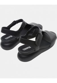 Sandali neri in pelle con cinturini regolabili, suola piatta e logo sulla soletta. Presentano una superficie liscia e un design semplice.