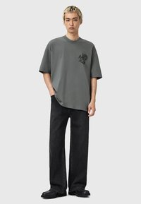 Szara, oversize'owa koszulka z logo, w połączeniu z czarnymi prostymi dżinsami i czarnymi butami. Casualowy materiał i luźny krój.