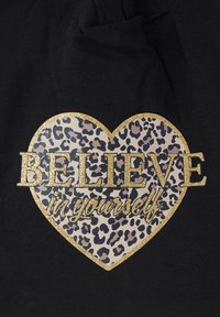 Czarna tkanina z złotym brokatowym sercem i wnętrzem w panterkę, z tekstem "WIERZ w siebie" w wyraźnym druku.