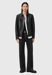 Veste en cuir noir avec deux poches poitrine, portée sur une chemise blanche et un débardeur noir. Associée à un jean noir à jambes larges et des chaussures vernis.