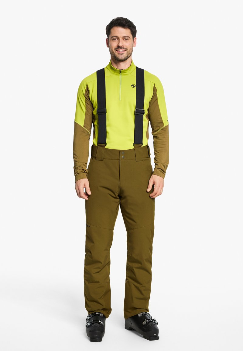 Männliche Skibekleidung mit einem leuchtend grünen Langarmunterhemd, dunkelbrownem Ärmeln und braunen Schneehosen mit schwarzen Trägern.