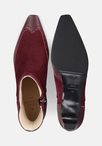 Bordeaux suede enkellaarzen met een spitse neus, decoratieve stiksels en een gladleren bovenwerk. De zool is plat en van rubber.