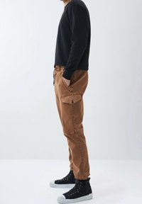 Bruna cargobyxor med sidofickor och smalnande ben, kombinerade med en svart långärmad tröja och svarta högskaftade sneakers.