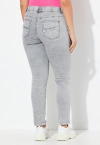 Šedé džíny skinny s hladkou texturou, dvěma zadními kapsami a mírně opotřebovaným designem. Nosené s bílými teniskami.