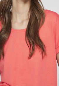 Korálově zbarvený krátký rukáv top s kulatým výstřihem, vyrobený z měkké tkaniny, s hladkou texturou a uvolněným střihem.