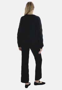 Maglione nero lavorato a maglia con maniche lunghe, abbinato a pantaloni larghi coordinati. Tessuto morbido e texturizzato, design minimale e scollatura rotonda.