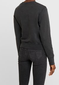 Felpa grigio scuro con scollo rotondo, polsini e orlo a coste. Tessuto morbido e strutturato. Abbinata a jeans skinny grigio scuro a vita alta.